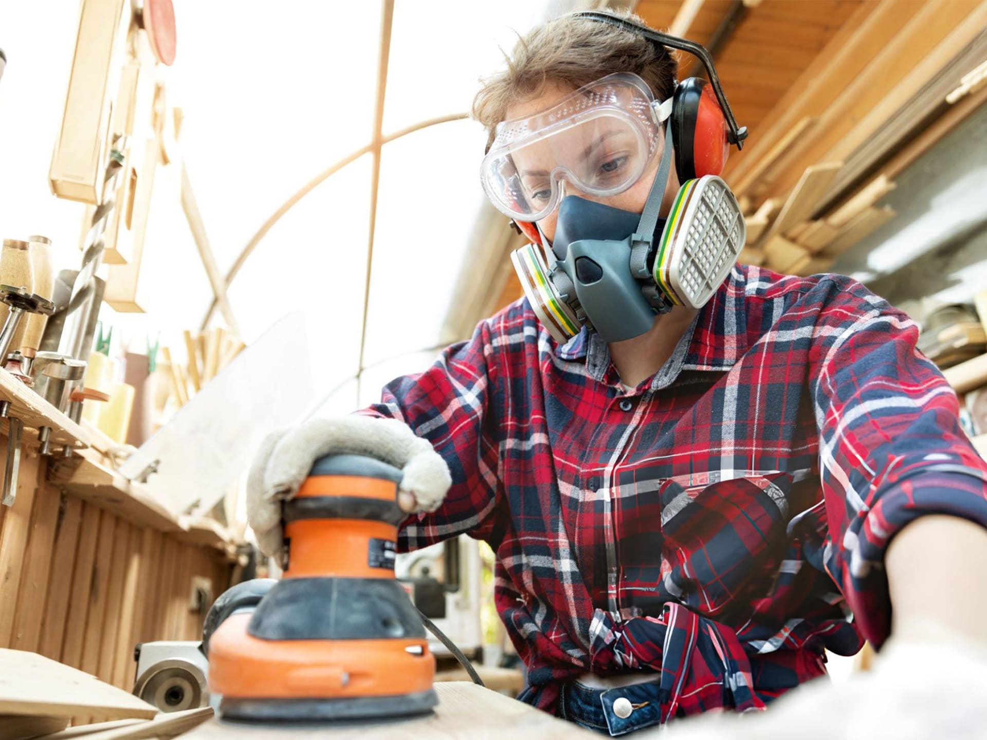 a woman wearing dust mask, eye protector and gloves is using an orbital sander